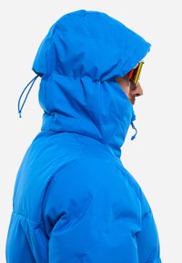 Blaue isolierte Jacke mit Kapuze und Zugband. Glattes, glänzendes Material, mit hohem Kragen und seitlichem Reißverschluss. Akzentuiert durch reflektierende Sonnenbrille.