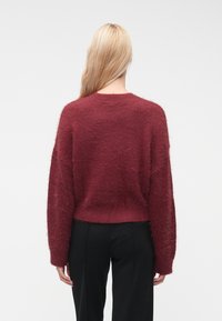 Μπουρντό, αφράτο πουλόβερ με κον�τό σχέδιο και μακριά, φαρδιά μανίκια. Η υφή είναι απαλή, με πλεκτό τελείωμα στο τελείωμα και τις μανσέτες.