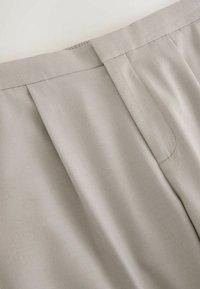Graues plissiertes Gewebe mit glatter Textur, flacher Taillenbund mit sauberem Finish, das das maßgeschneiderte Design und den weichen Fall hervorhebt.