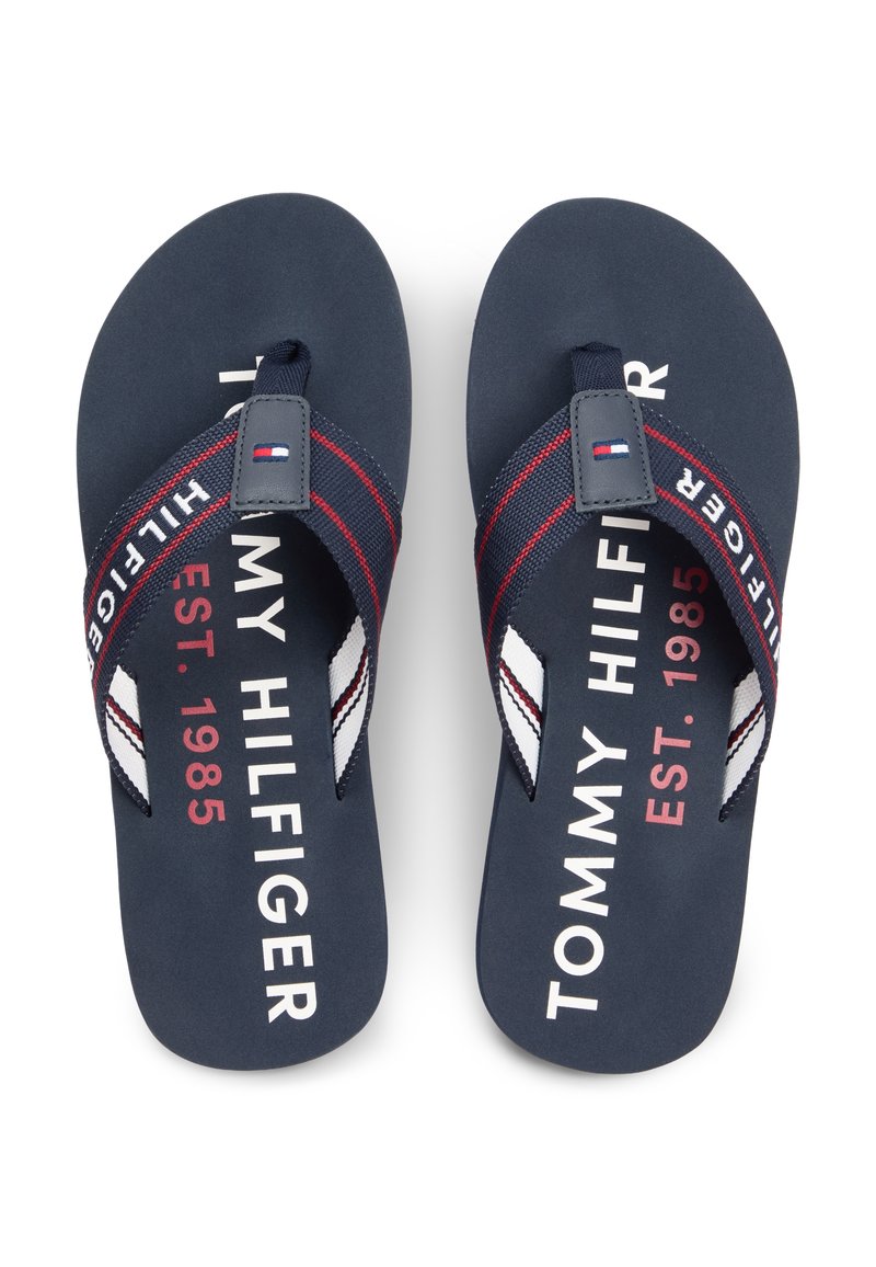 Chanclas Tommy Hilfiger azul marino con tiras de tela a rayas rojas y blancas y texto de marca en las plantillas y las tiras.