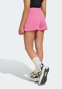 Rosa idrottsshorts med en avslappnad passform, som har en bred elastisk midjeband och sidofickor, parat med vita och pastellgradient-strumpor samt svarta sneakers.