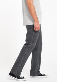 Vaqueros de mezclilla gris con un corte recto, que presentan un pequeño detalle de agujero, combinados con zapatillas de lona negras y una camiseta gris.