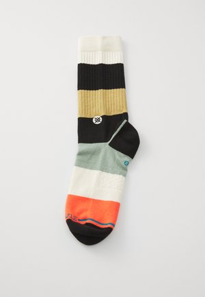 Calcetines multicolores con rayas verticales en negro, beige, blanco, verde y naranja. Incluyen un detalle de logo en el costado. Textura acanalada.