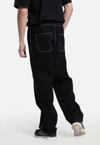 Pantaloni in denim nero con cuciture bianche, dotati di una vita elastica e tasche posteriori. La vestibilità è ampia con un design delle gambe affusolato.