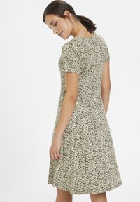 Short-sleeve dress in olive green with a white floral pattern, A-line shape, and soft fabric, featuring a round neckline and knee-length hem.