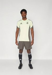 Nogometna uniforma Adidas v svetlo zeleni barvi s temno sivimi poudarki, ujemajočimi kratkimi hlačami in črnimi nogavicami z belimi črtami.