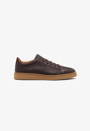 Zapatilla de cuero marrón con detalles perforados, superficie texturizada, cordones marrones y una suela de goma de color marrón claro. Diseño minimalista.