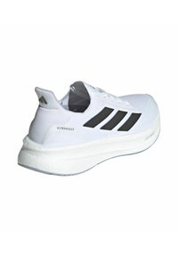 Weißer Sportschuh mit einem strukturierten Strick-Obermaterial, schwarzem Drei-Streifen-Logo und einer dicken weißen Zwischensohle mit "ULTRABOOST"-Branding an der Ferse.
