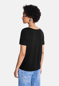 T-shirt noir texturé avec un col rond et des manches courtes retroussées, associé à un jean en denim bleu clair.