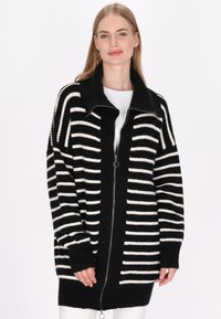 Černobílý pruhovaný cardigan na zip s vysokým límcem, pletenou strukturou a volným střihem. Obsahuje dlouhé rukávy a boční kapsy.