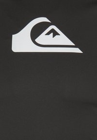 Black fabric featuring a prominent white Quiksilver logo, shaped like a wave above a mountain, with smooth texture and matte finish.