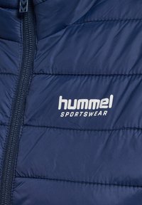Granatowa pikowana kurtka sportowa z pionowym zamkiem błyskawicznym i białym logo „hummel SPORTSWEAR” na lewej części klatki piersiowej.