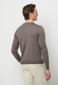 Maglione marrone lavorato a maglia con scollo rotondo, maniche lunghe e polsini a coste, abbinato a pantaloni chiari. Tessuto liscio e forma aderente.