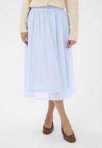 Světle modrá sukně ke kolenům z průsvitné, splývavé látky s elastickým pasem. Nošena s hnědými tkanými vzorovanými botami.