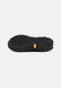 Fekete gumitalp mély barázdákkal, kiemelkedő sárga Vibram logóval. Tartós kivitelezés a tapadás és a stabilitás érdekében.