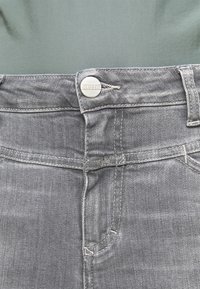 Jeans de mezclilla gris con botón plateado etiquetado como "CLOSED", costuras visibles y apertura de bolsillo frontal. Textura suave con ligero desgaste.