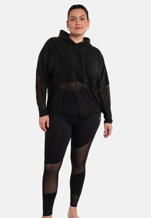 Schwarzer Kapuzenpullover mit transparenter Overlay und elastischem Saum, kombiniert mit schwarzen Leggings mit Mesh-Akzenten und geometrischem Muster.
