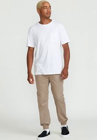 Biała koszulka z krótkim rękawem i kieszenią na piersi, zestawiona z beżowymi zwężanymi spodniami i czarnymi wsuwanymi butami. Prosty, casualowy design.