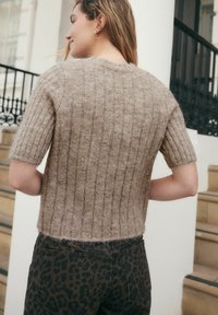 Maglione a maniche corte, a coste, in materiale di maglia marrone chiaro con una texture pelosa, abbinato a pantaloni con stampa leopardata scura.