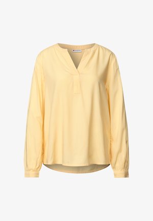 Gul långärmad blus med V-ringning, samlade manschetter och en avslappnad passform. Tillverkad av mjukt tyg med minimala designdetaljer.