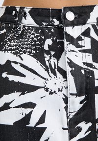 Mustikka-valkoisella kukkakuosisella denimmillä, jossa on korkeavyötäröinen muotoilu. Varustettu nappikiinnityksellä ja teksturoidulla kankaalla.