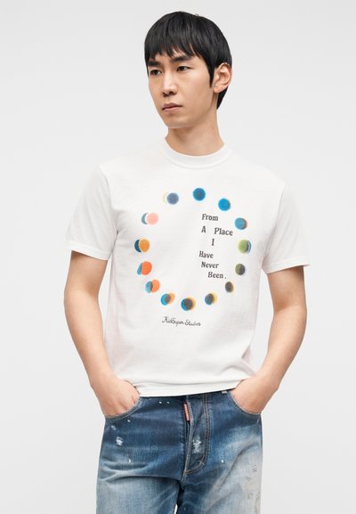 Λευκό βαμβακερό μπλουζάκι με κυκλικό σχέδιο πολύχρωμων κουκίδων και το κείμενο «From A Place I Have Never Been» σε μαύρο χρώμα.