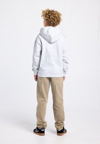 Grijze hoodie met capuchon, losse pasvorm, katoenen materiaal. Gecombineerd met beige broek en zwarte sneakers met gumzool. Eenvoudig ontwerp, zonder patronen.