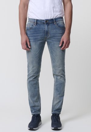 Los jeans de mezclilla azul claro presentan un corte slim, un lavado desvaído, un diseño de cinco bolsillos y costuras en contraste. Se llevan con zapatillas oscuras.