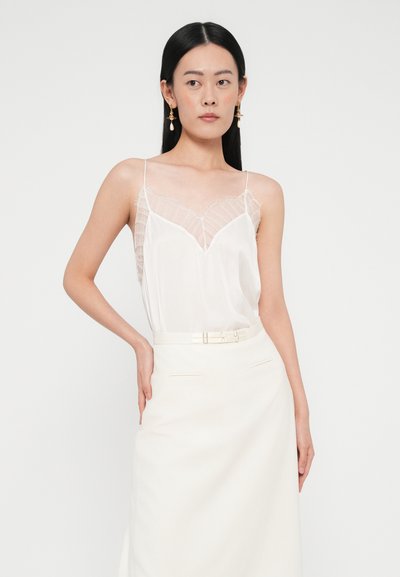 Caraco en satin blanc avec bordure en dentelle et fines bretelles, associé à une jupe blanche taille haute avec ceinture et détails minimalistes.