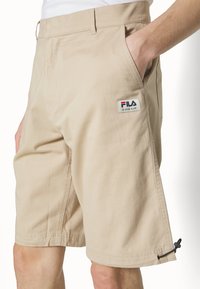 Shorts beiges en coton avec une coupe droite, dotés de poches latérales et d'un petit logo Fila sur le côté gauche. Système de réglage au bas.