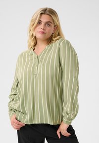Ljusgrön blus med vertikala vita ränder, lätt material, knäppning fram, långa ärmar och en avslappnad passform.