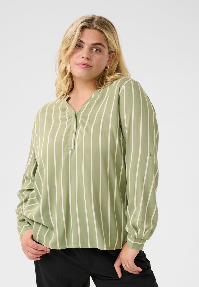 Ljusgrön blus med vertikala vita ränder, lätt material, knäppning fram, långa ärmar och en avslappnad passform.