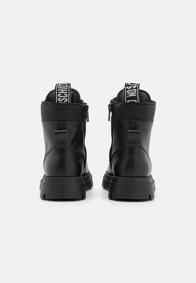 Bottines en cuir noir avec une semelle épaisse à crampons, dotées d'une fermeture éclair et d'une boucle en tissu avec un logo blanc à l'arrière.