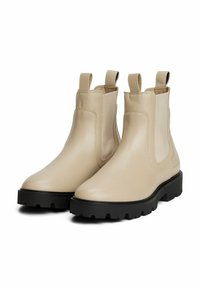 Botas Chelsea de cuero beige con paneles laterales elásticos, tiradores y suelas de goma negra texturizada, que presentan un diseño elegante y aerodinámico.