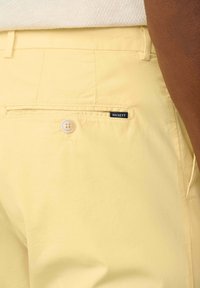 Gule bomuldsshorts med en enkelt baglomme, hvid knaplukning og et sort "HACKETT" label. Glat tekstur og skræddersyet design.