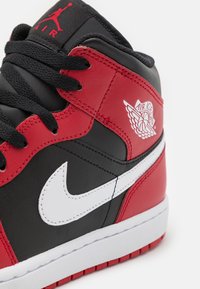 Sneaker alta in pelle nera con accenti rossi e bianchi. Presenta un prominente swoosh bianco Nike e il logo dell'ala Air Jordan. Lacci neri.