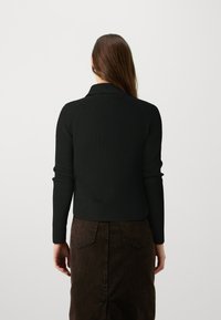 Pull en tricot noir à côtes avec un col, manches longues ajustées et ourlet court, associé à une jupe en jean marron avec poches arrière.