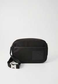 Črna pravokotna torbica za čez ramo z žepom z zadrgo spredaj, nastavljivim trakom in vtisnjenim logotipom Lacoste.