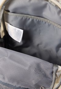 Εσωτερικό σακιδίου πλάτης με επένδυση από γκρι ύφασμα, που διαθέτει τσέπη από δίχτυ και ετικέτα φροντίδας. Ο σχεδιασμός είναι λειτουργικός με λείο υφή.