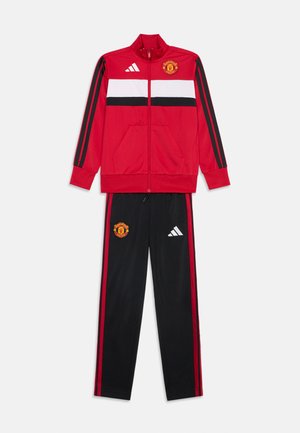 Survêtement de sport rouge et noir de Manchester United avec veste zippée comportant des bandes blanches et noires et pantalon assorti avec des bandes latérales rouges.