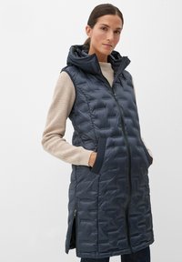 Marineblauer, gesteppter ärmelloser Puffer-Westen mit Kapuze, ausgestattet mit einem Reißverschluss vorne, zwei Seitentaschen und einem gerippten Pullover darunter.