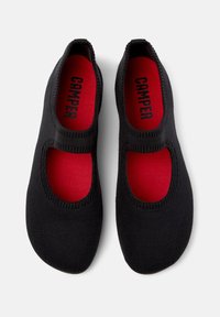 Svart stickad balettklack med utskärningar och röda insoles med "CAMPER"-logotyp. Mjuk textur med elastiska kanter för komfort.