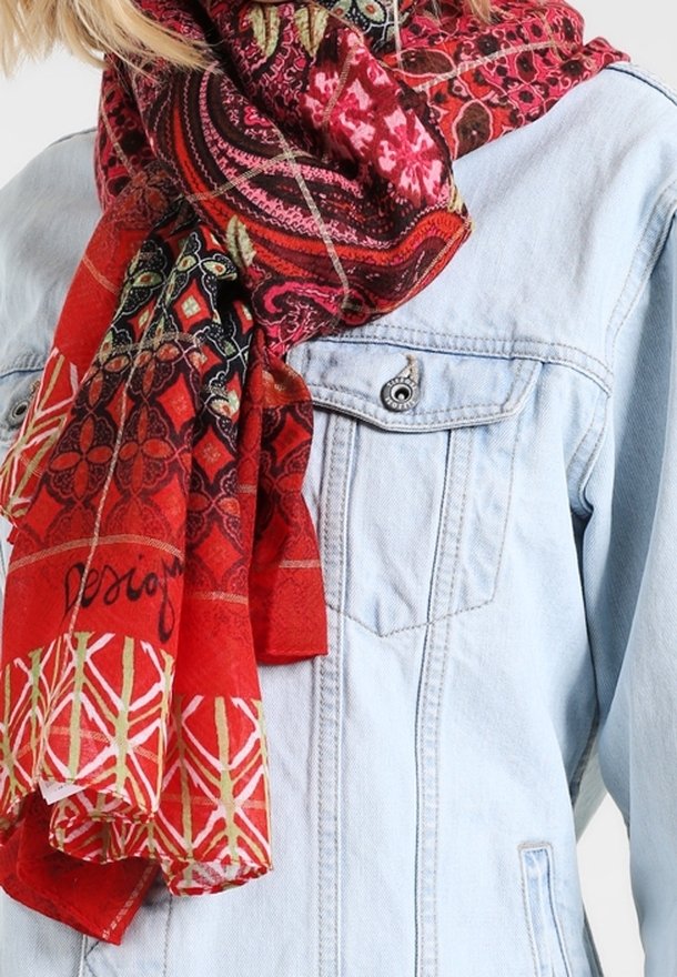 Femme portant une écharpe rouge à motifs enroulée autour du cou sur une veste en denim bleu clair avec des poches poitrine.