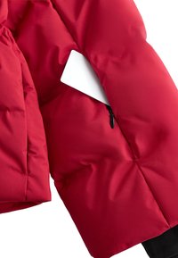 Piros felfújható dzseki, sima anyagból, cipzáras zsebbel és a zsebben részben látható fehér kártyával. Texturált, szigetelt kialakítás.