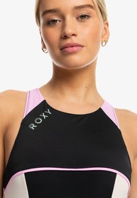 Black sports top with pink accents, featuring a round neckline and Roxy logo. Made of stretchy, smooth material with contrasting seams.