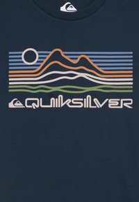 Jūras spēku t-krekls ar stilizētu kalnu grafiku oranžā, zilā un zaļā krāsā, ar sauli un tekstu "Quiksilver" baltā krāsā apakšā.