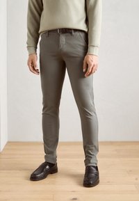 Pantaloni slim-fit verdi realizzati in misto cotone, con frontale piatto, passanti per cintura e tasche laterali, abbinati a mocassini in pelle nera.