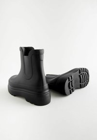 Bottes chelsea en caoutchouc noir avec une finition lisse, des panneaux latéraux élastiques et des semelles en caoutchouc texturé avec un grip à motifs.