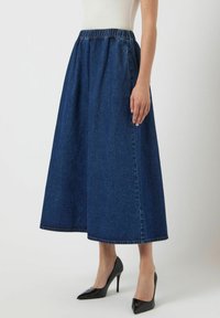Jupe midi en denim avec une taille élastique, couleur bleu profond, forme A-line fluide et accents de couture visibles à l'ourlet.