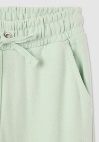 Jasnozielone dresy z elastycznym pasem w talii i sznurkiem do regulacji, bocznymi kieszeniami oraz miękkim, teksturowanym materiałem.